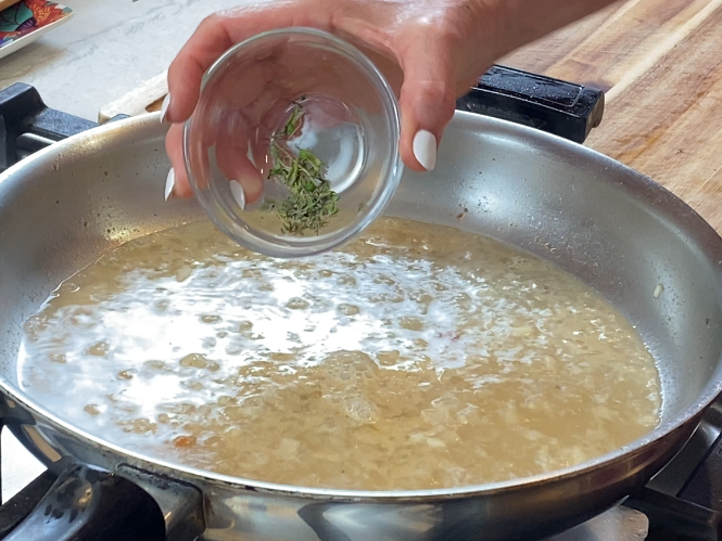 Fresh thyme being added to a simmering pan sauce