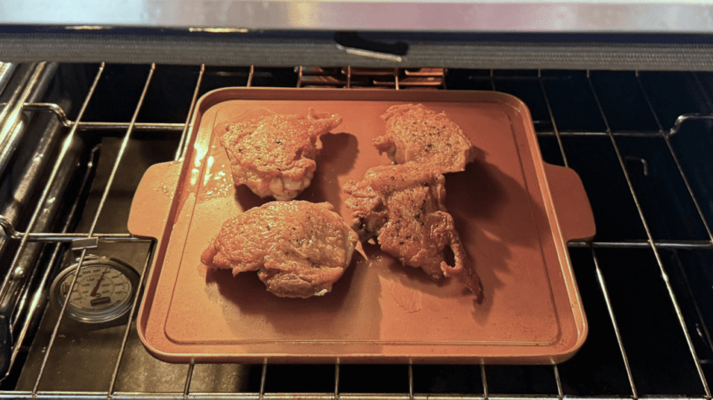 Seared chicken thighs finishing in a 375°F oven on a sheet pan