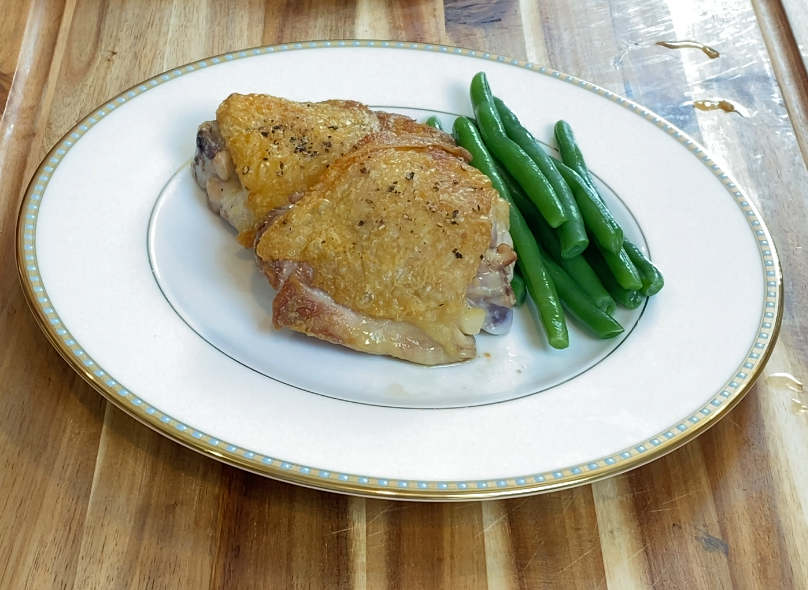 Crispy bone-in chicken thighs with golden skin served with green beans on a white plate