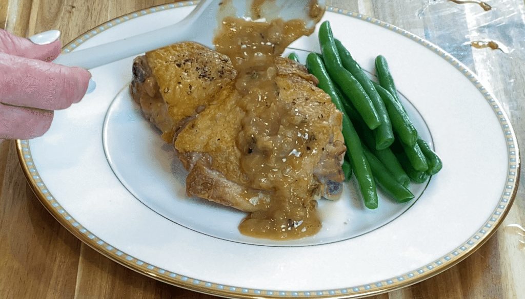 Pan sauce being spooned over a golden seared chicken thigh with green beans
