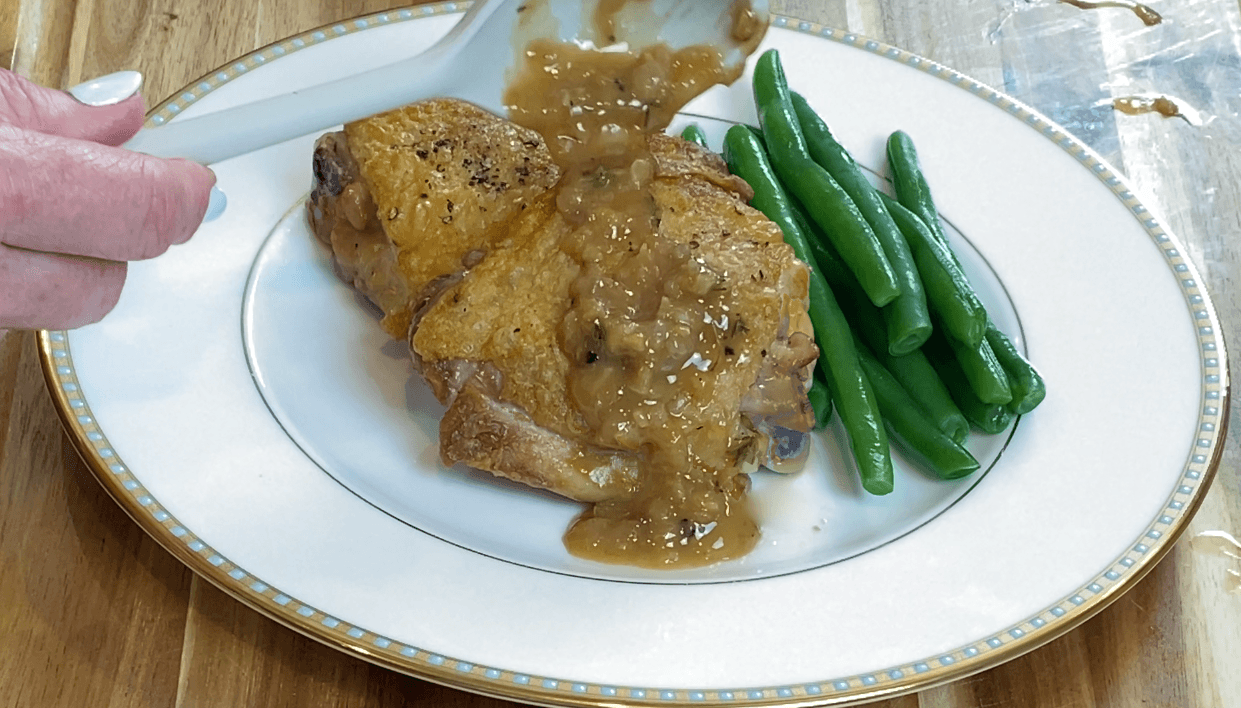 Pan sauce being spooned over a golden seared chicken thigh with green beans