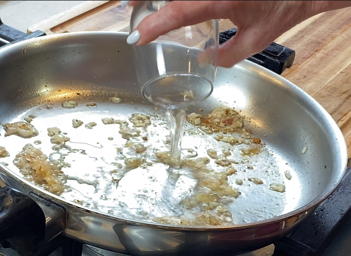 White wine being poured into the pan to deglaze the fond