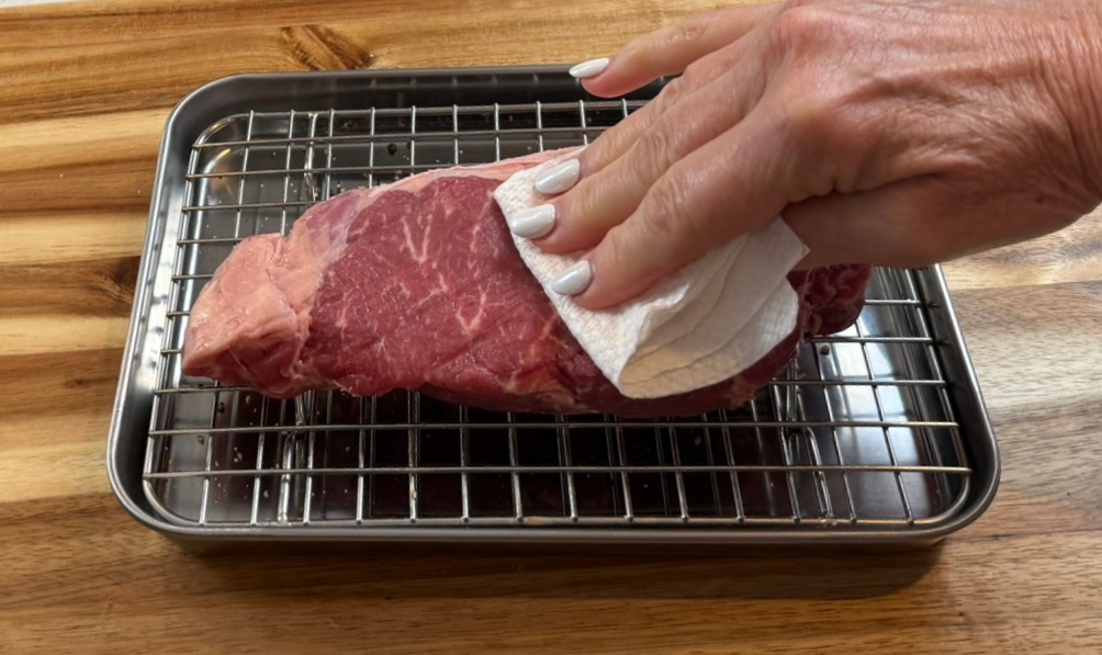 Patting a raw NY strip steak dry with paper towels before searing