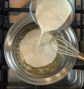 Cold heavy cream being poured into warm melted butter in a saucepan