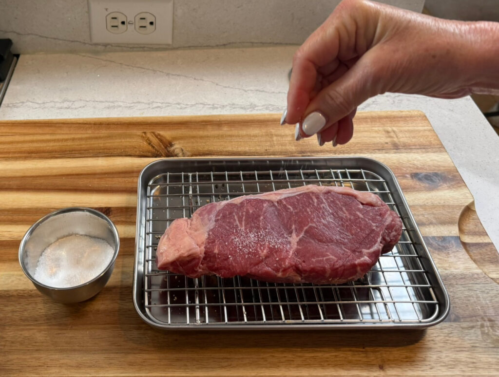 Seasoning a raw steak with kosher salt before cooking