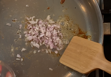 Finely minced shallots softening in a pan with fond