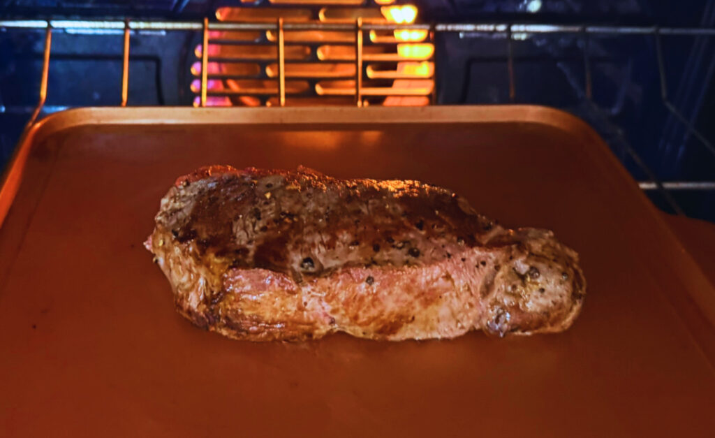 Seared steak finishing in a 400 degree oven on a baking sheet