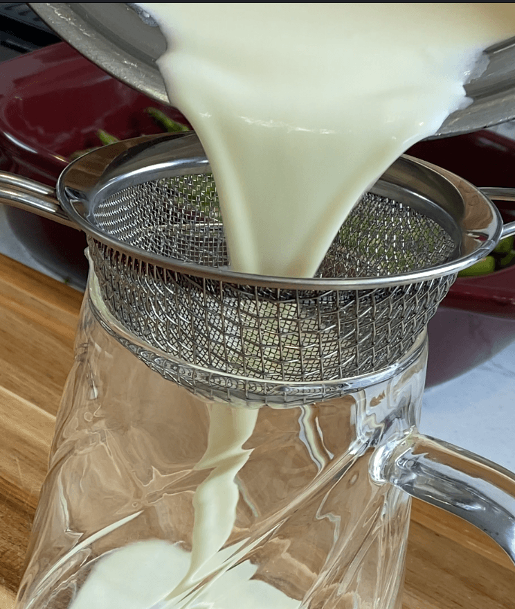 The cream sauce formula being finished through a fine-mesh strainer to remove the aromatics