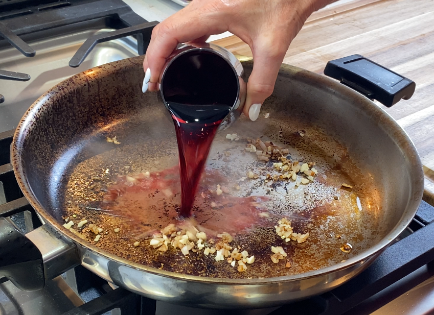 Red wine being poured into a hot skillet to deglaze the fond for a red wine pan sauce