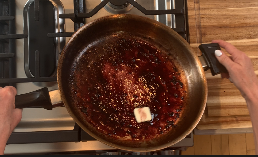 Cold butter being swirled into a red wine reduction sauce to finish and emulsify