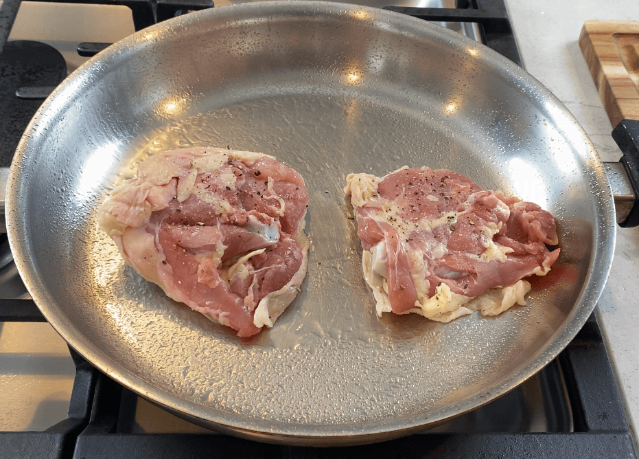 Chicken thighs searing skin-side down in a stainless steel pan