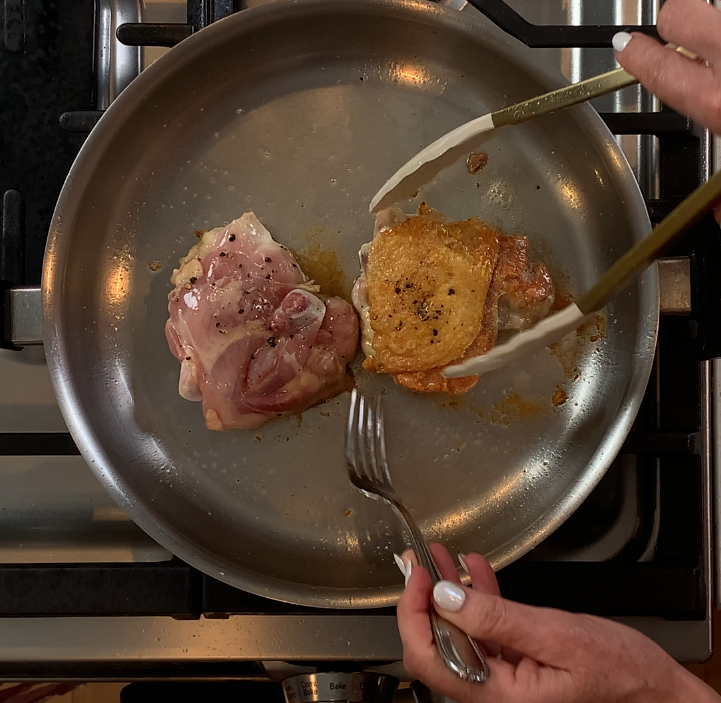 Flipping chicken thighs in the pan, one side golden brown
