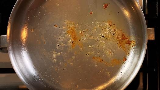 Browned bits of fond stuck to the bottom of a stainless steel pan after searing chicken
