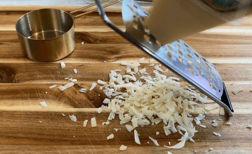 Freshly grating parmesan from a wedge, using a microplane, onto a wooden cutting board