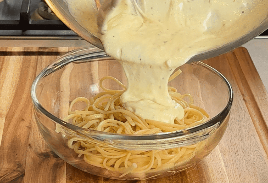 Silky garlic parmesan cream sauce being poured over linguini in a glass bowl
