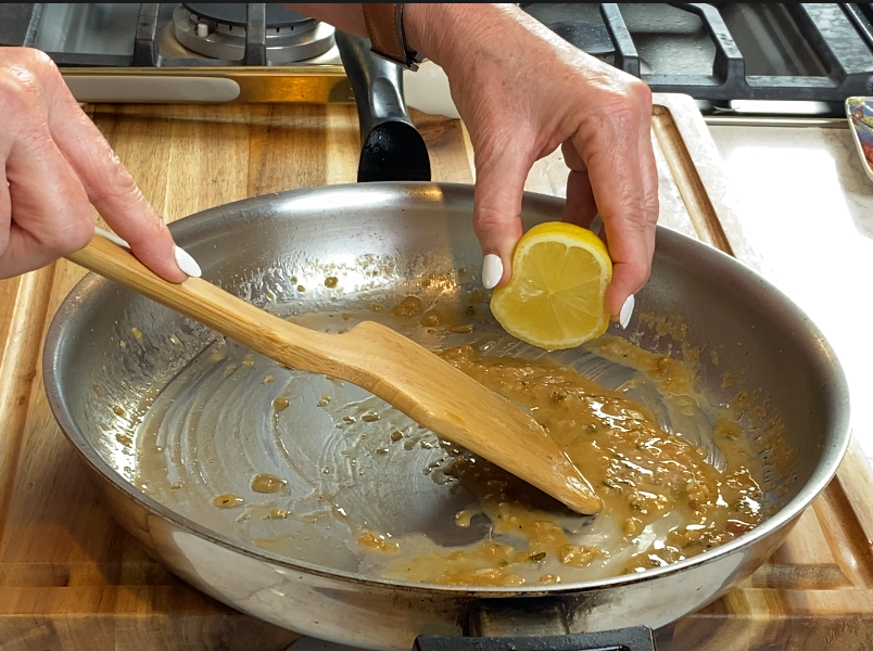 A squeeze of fresh lemon being added to the finished pan sauce