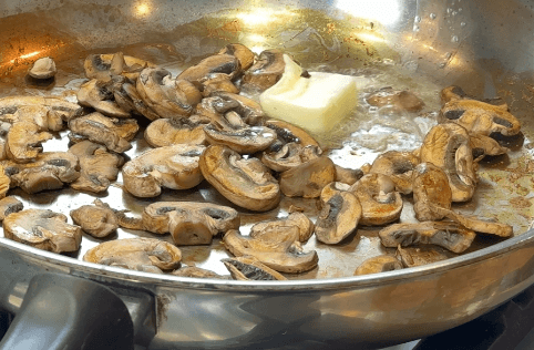 Sliced mushrooms browning in butter in a stainless steel pan