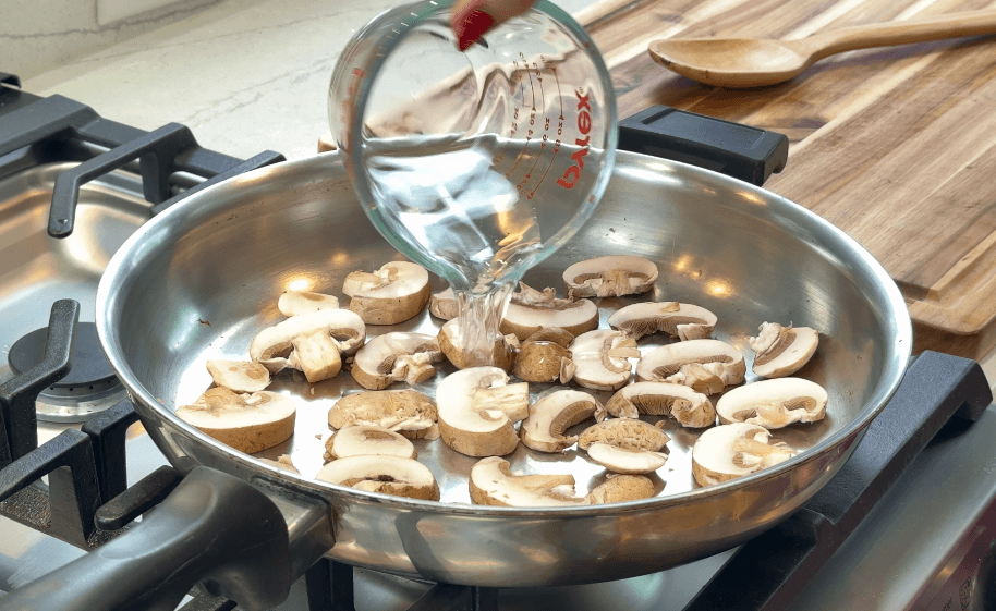 Pouring water into a cold pan with sliced raw mushrooms to start the cooking process.