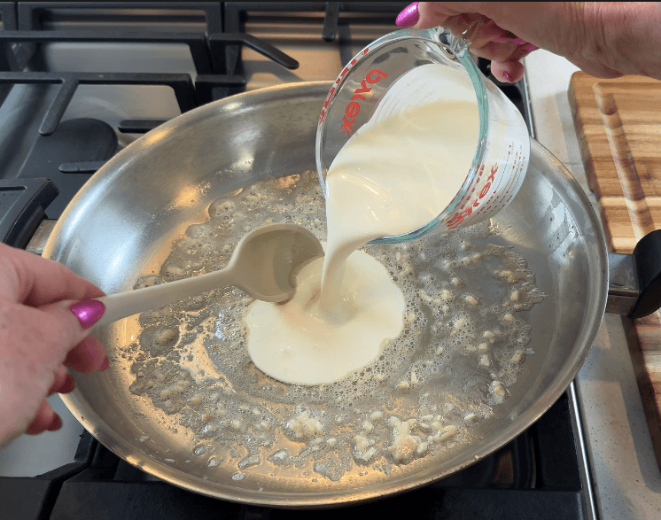 Pouring cold heavy cream into a pan with garlic and butter to start the sauce base