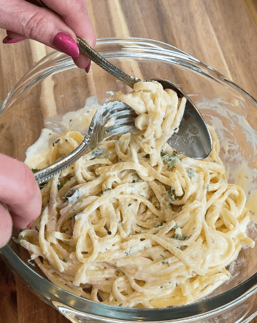 Garlic parmesan cream sauce coating linguini with fork and spoon serving from a glass bowl