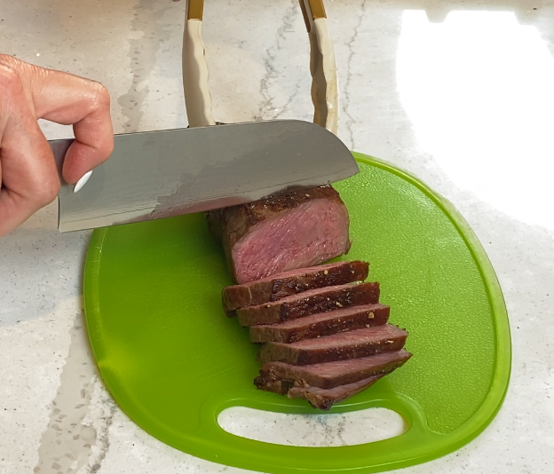 Slicing a rested steak against the grain on a cutting board