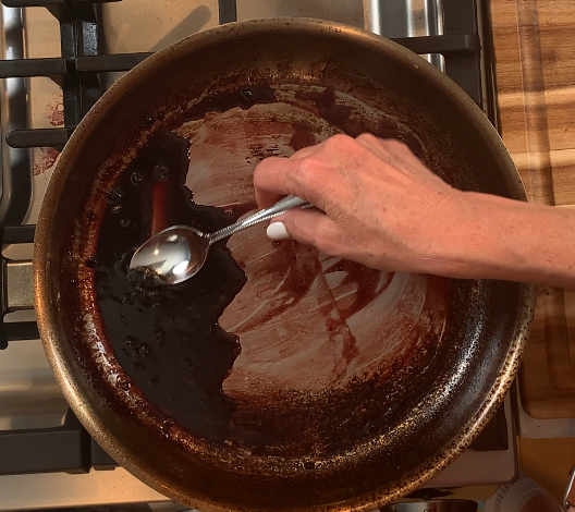 Testing a red wine shallot reduction sauce with a spoon to check consistency