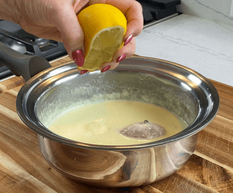 A wedge of fresh lemon being squeezed into a finished cream sauce off the heat