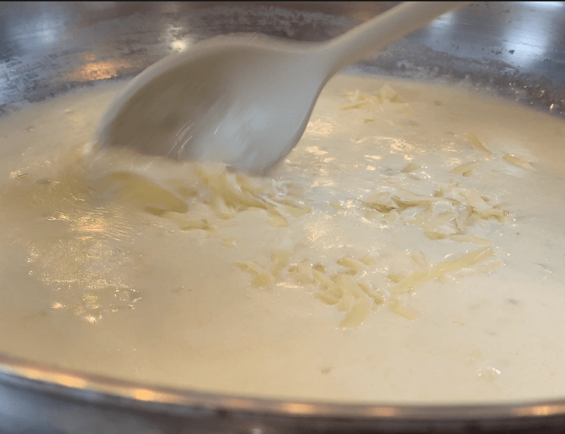 Stirring freshly grated parmesan into cream sauce until it fully melts in