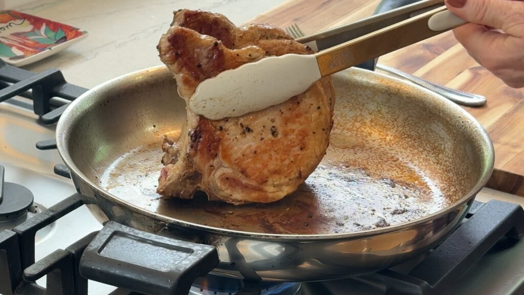 Searing the fat cap of a pork chop on its side with tongs