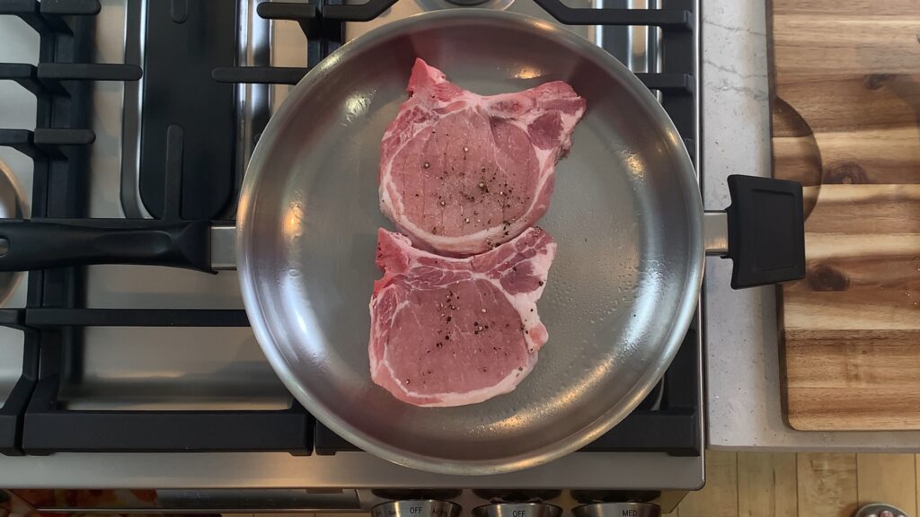 Bone-in pork chops searing undisturbed in a stainless skillet