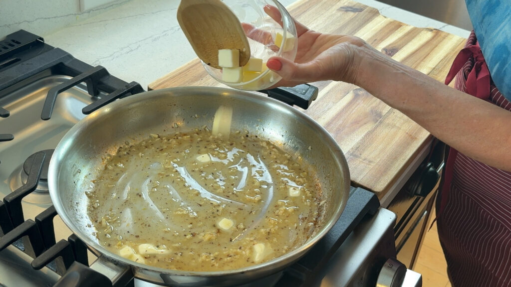 Cold butter being whisked into lemon sauce to create a silky emulsion