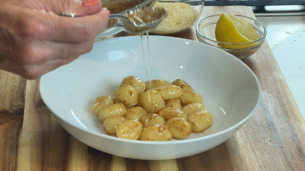 Adding extra brown butter sauce to a bowl of gnocchi.