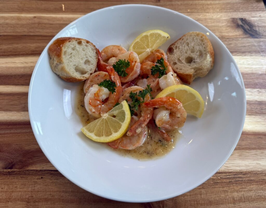 Lemon butter sauce with shrimp, parsley, and lemon wedges served with crusty bread