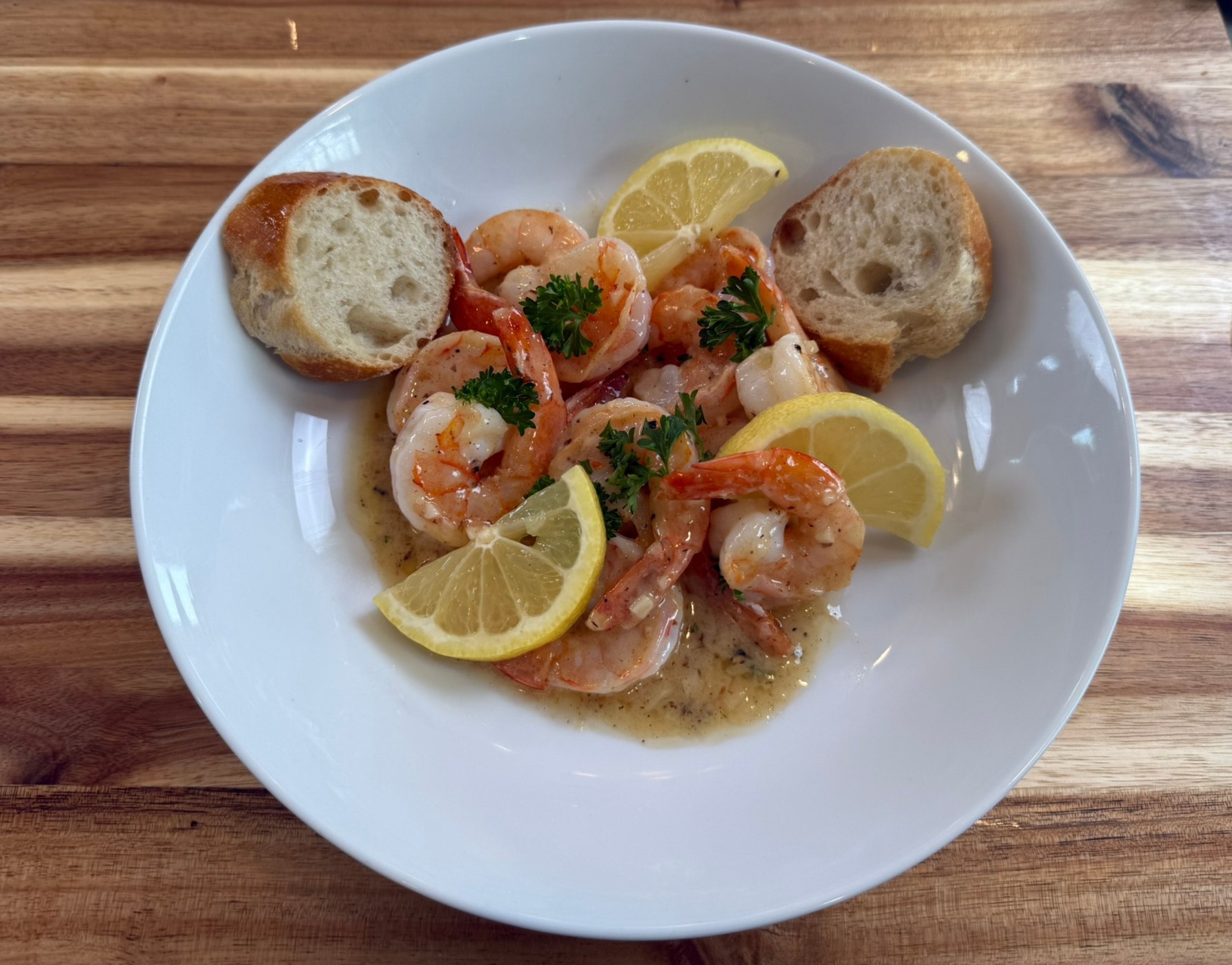 Lemon butter sauce with shrimp, parsley, and lemon wedges served with crusty bread