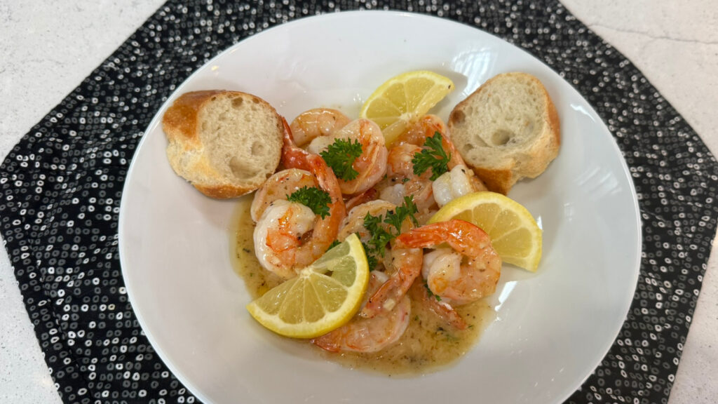 Lemon butter sauce with shrimp, parsley, and lemon wedges served with crusty bread