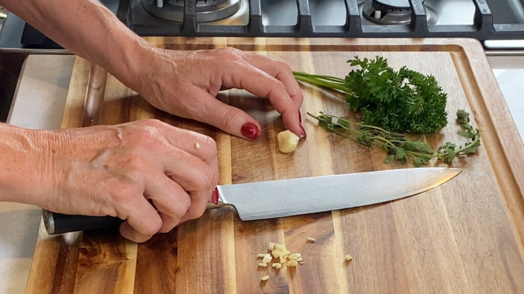 View of rough-chopped garlic, parsley, and oregano on a cutting board