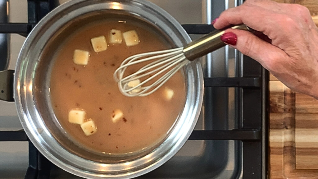 Whisking cold butter into warm vinegar base to mount the sauce"