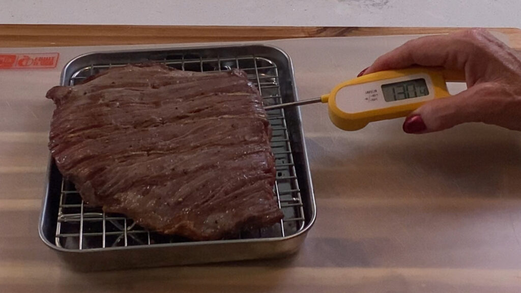 Meat thermometer checking flank steak temperature for medium-rare