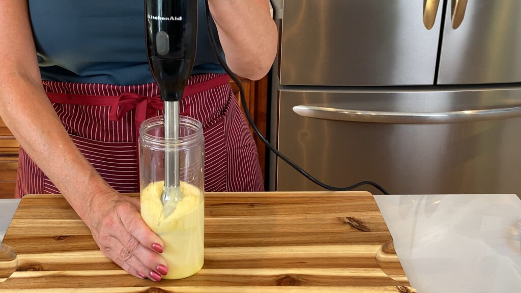 Immersion blender in the container, emulsion visibly forming.