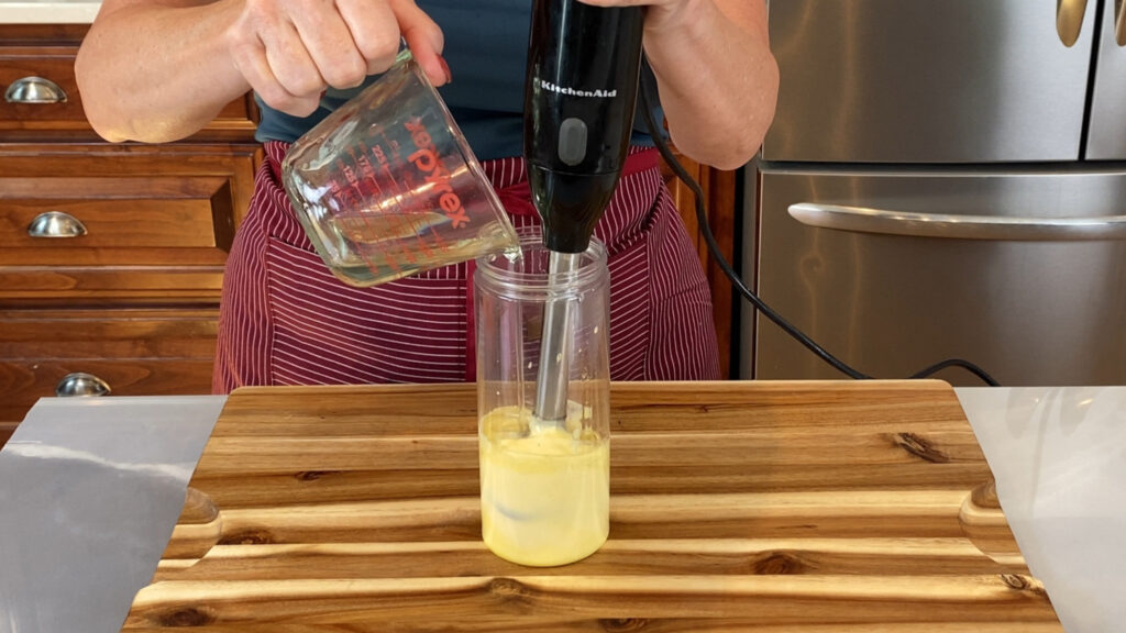 Making mayonnaise mid-emulsification view of immersion blender while adding the oil to egg yolk, acid and mustard. 