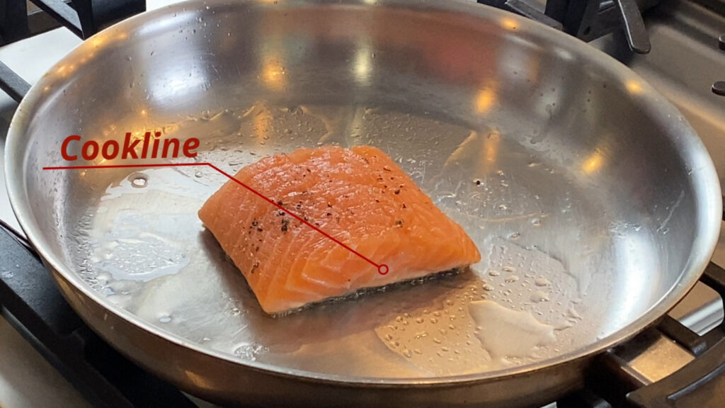 Salmon fillet skin-side down in pan searing. Overlay image of the cookline being demonstrated.