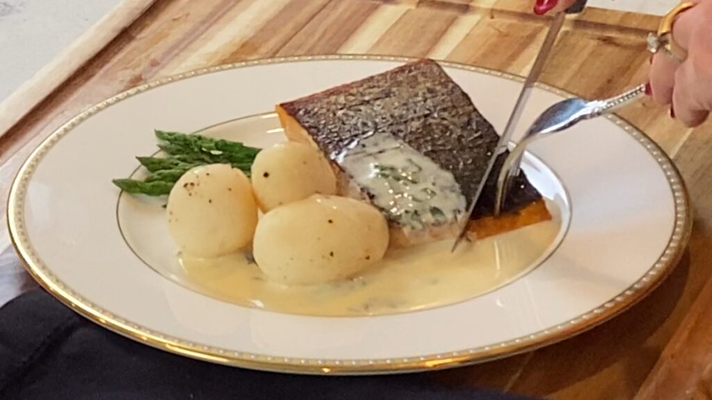Salmon being sliced on a plate with Norwegian butter sauce, potatoes, and asparagus.