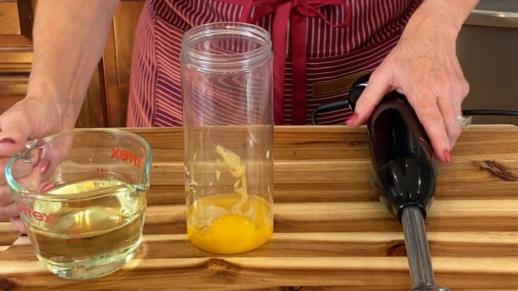 Yolk, mustard, and acid together in the container, before oil is added and blended with an immersion blender.