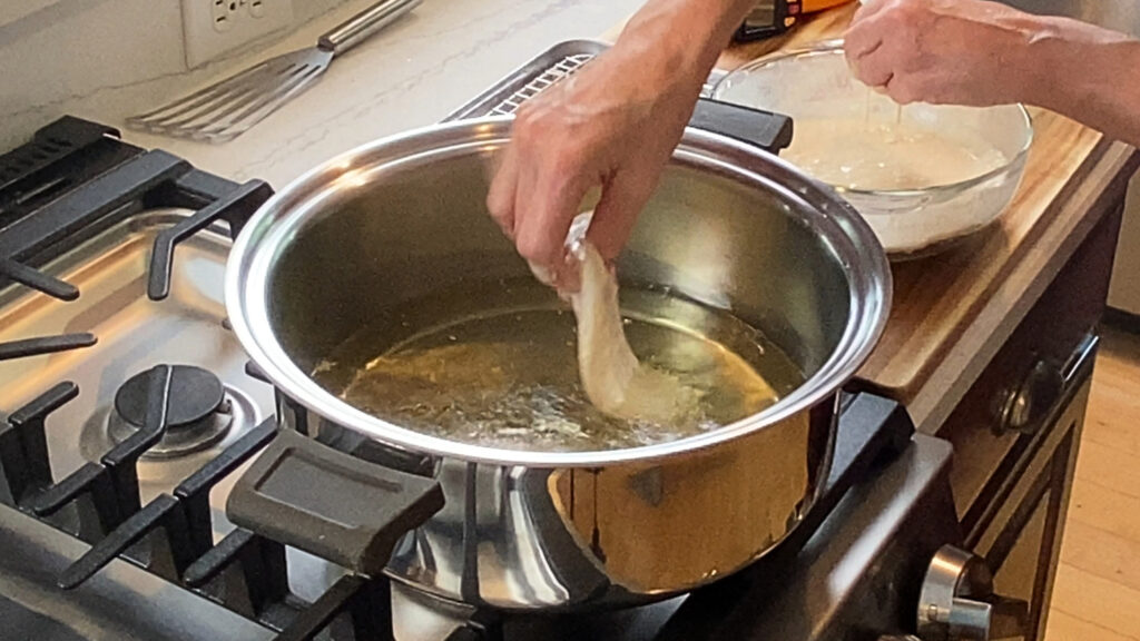Battered cod entering the hot oil, batter visibly puffing