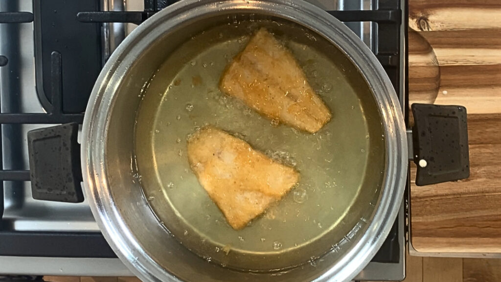 Beer battered cod cooking in hot oil. 